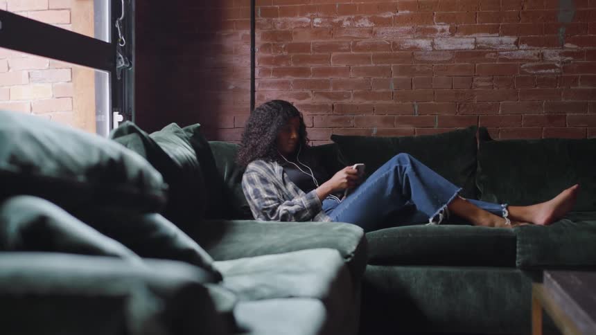 Woman relaxes on the couch while using her phone with headphones