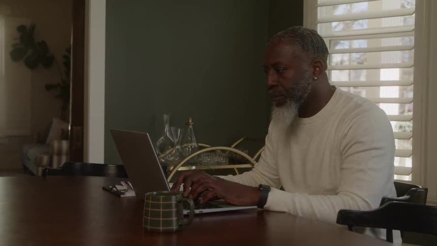Man sitting at a table typing on a laptop computer