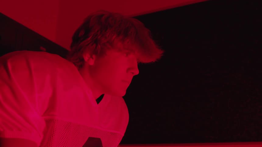 Young man wearing a football jersey in a room filled with red light looks up
