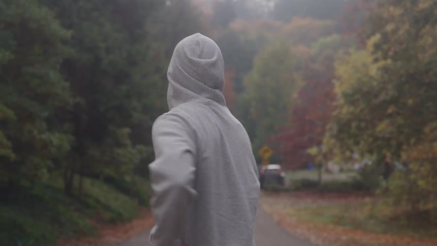 Person from the back wearing a grey hoodie stretching on a road surrounded by trees outdoors during day time