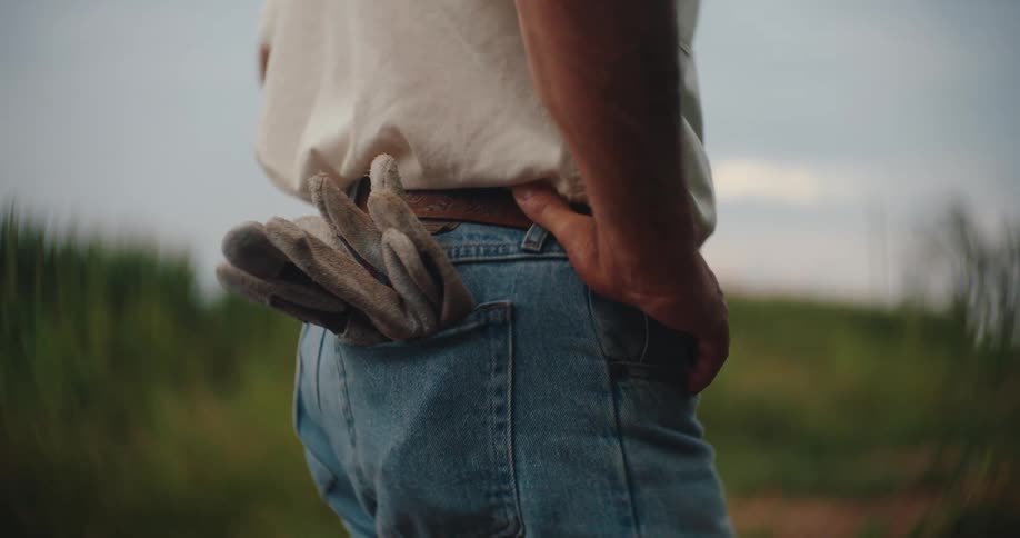 Man rests his hand on his hip with work gloves tucked into his jeans pocket
