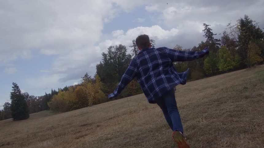 Boy runs across an open field with his arms extended while moving through the dry grass