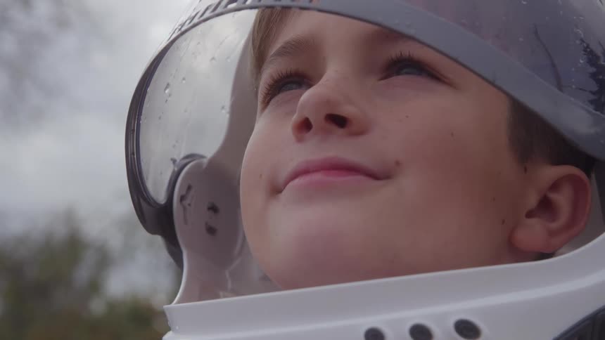 Boy smiles while looking at the sky wearing a space suit helmet