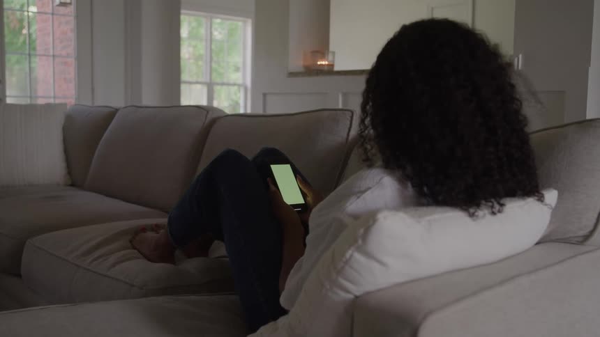 Woman sitting on the sofa views the smartphone she is holding during the daytime