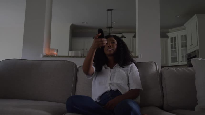 Bored woman sitting on the couch at home turns on the television with her remote