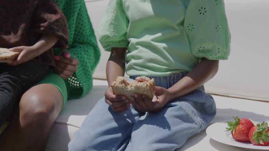 Children sitting and holding sandwiches on a sunlit bench
