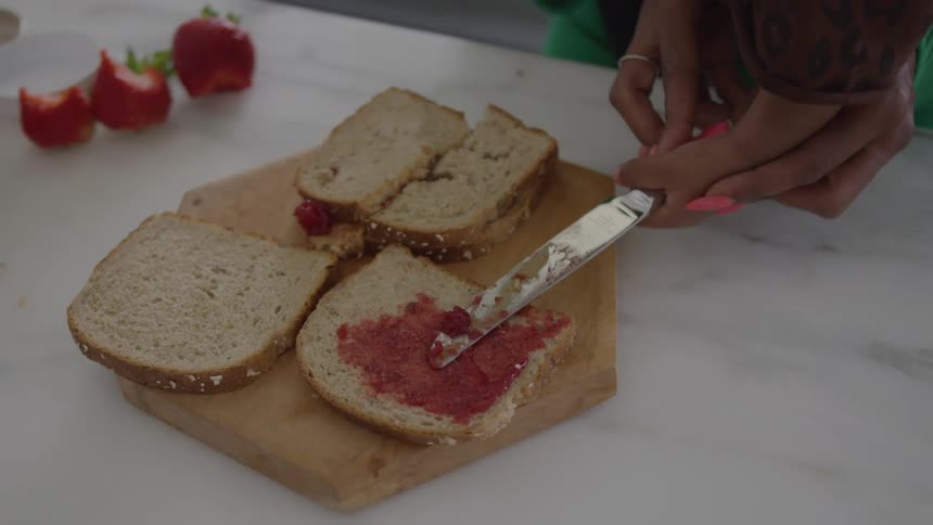 The woman and child spread strawberry jam on bread