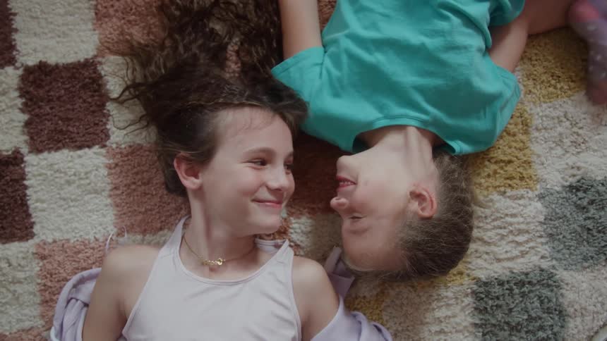 Two children lying on the rug smile while resting side by side