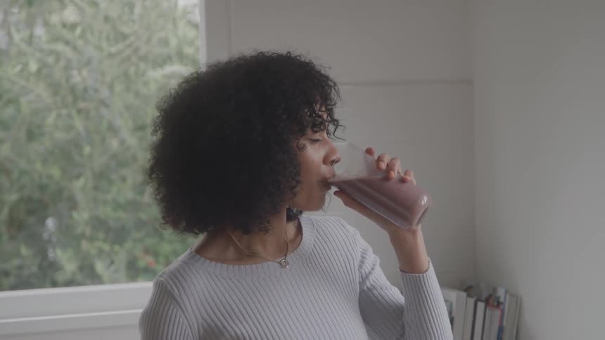 Woman standing at home near her desk sips a drink during the daytime