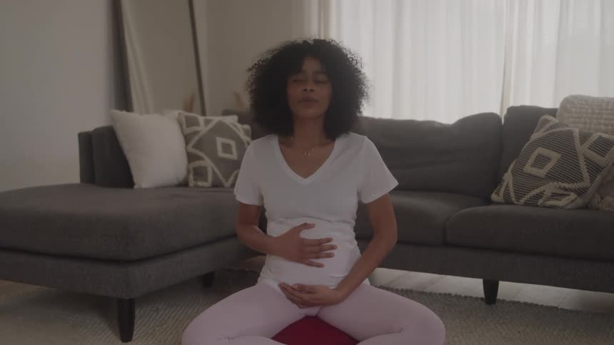 Woman sitting on the rug practicing breathing with her hands on her abdomen