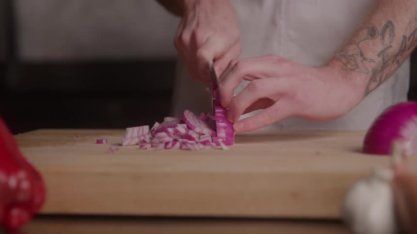 Close up of a male chef cutting and chopping onions on a wooden chopping board in the kitchen