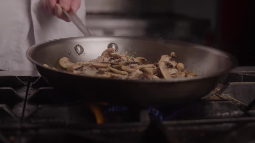 Mushrooms being sauted while seasoning is added to the pan