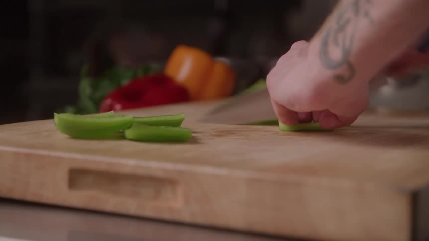 Cook slicing celery stalks into strips on the board