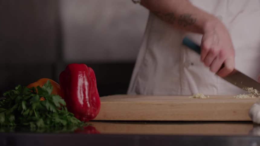 Cook chopping garlic on the board beside bell peppers and parsley