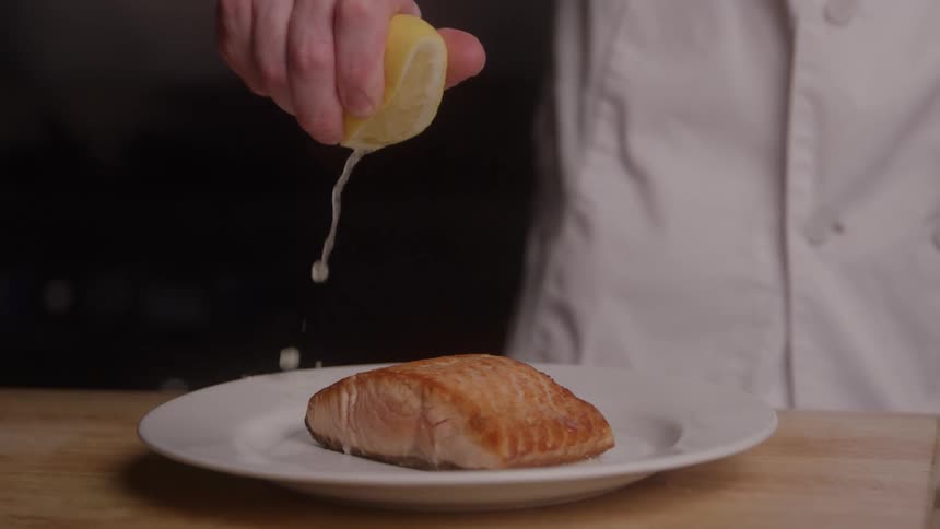 Close up of a male chef adding a fresh lemon twist to a protein dish on a table