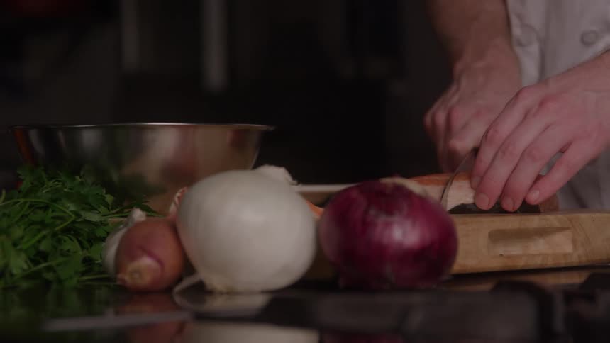 Person slicing vegetable on wooden board surrounded by fresh ingredients in professional kitchen setting