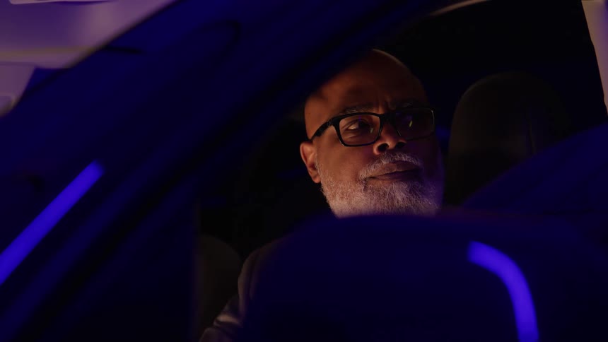 Graybearded man looking through the windshield under purple light
