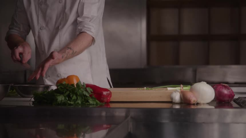 A male chef adding chopped vegetables from a chopping board to a frying pan while preparing food in a kitchen