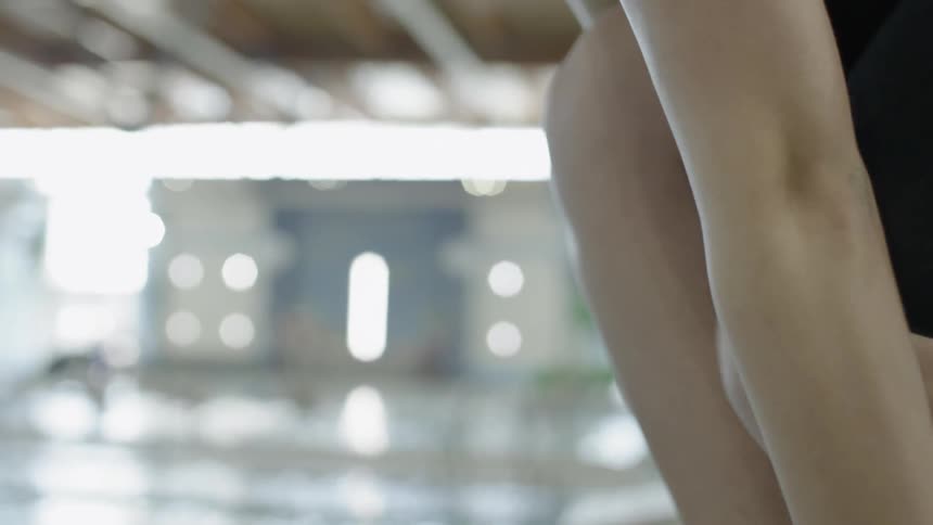A woman climbing onto a diving board by an indoor pool