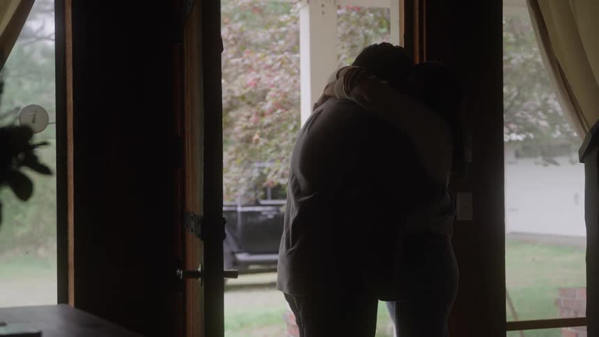A woman and a man are embracing indoors near a glass door