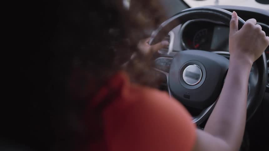 Woman driving an automobile moving to the music as she holds the steering wheel