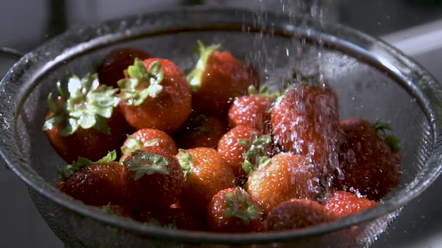 Strawberries being rinsed in the strainer under running water