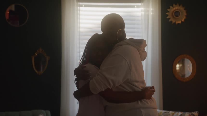 Mother and daughter hugging each other while standing in a living room during daytime