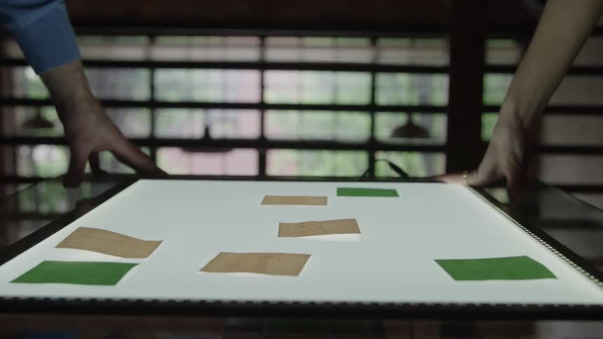 Two people arrange brown and green sticky notes on an illuminated light table