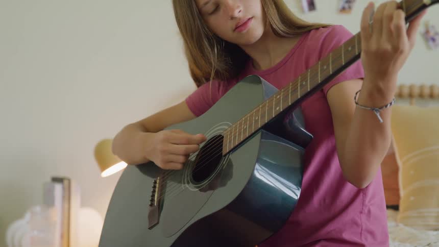 Girl practicing guitar in the bright bedroom