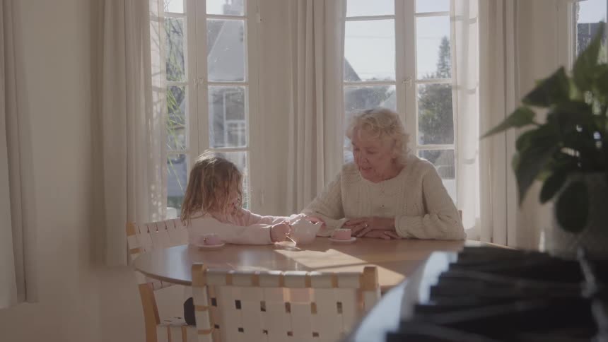 Elderly woman sitting at the table interacting with a child in a sunlit room