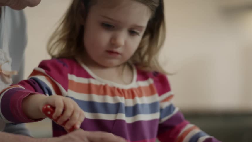 A woman holds a cupcake while a girl adds more frosting
