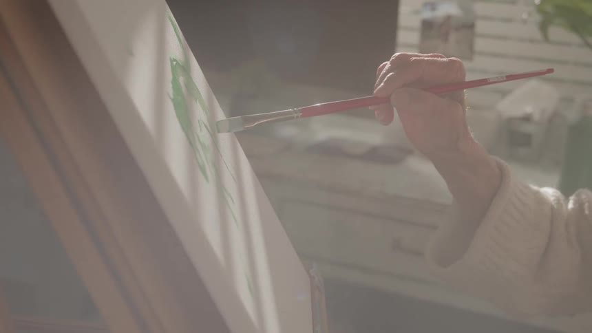 Woman holds a paintbrush as she paints on canvas on an easel