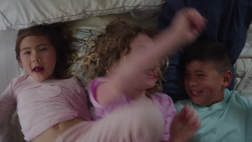 Three children lying on white bed interacting playfully