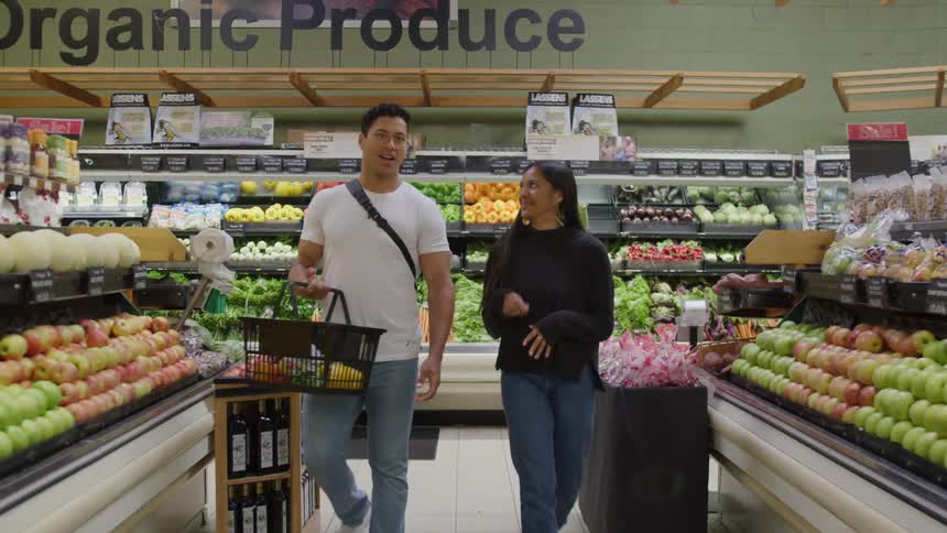 Two people talking in grocery produce section surrounded by organic fruits and vegetables