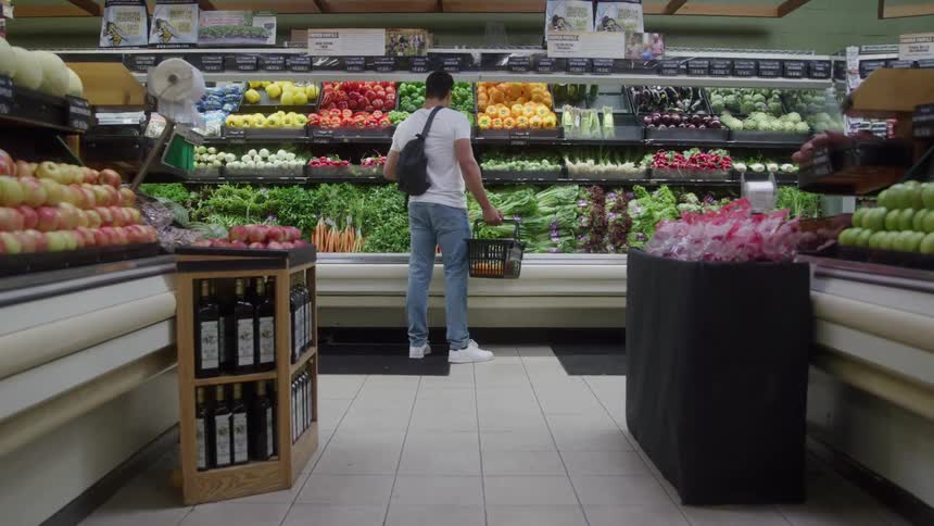 A man carrying a shopping basket is in a supermarket in the vegetable section