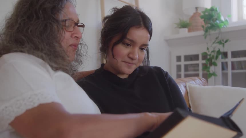 An adult woman with a book in her hand is reading to a young girl sitting next to her