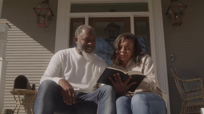 Two people seated on house steps share a quiet intimate moment reading together