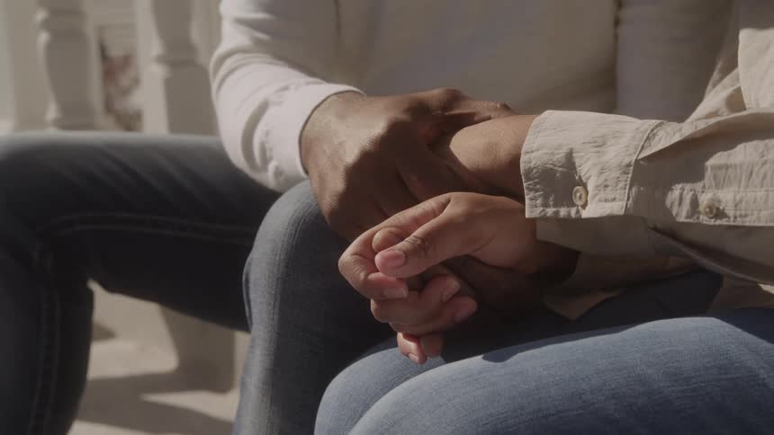 A couple sits closely together tenderly holding hands in a moment of quiet connection