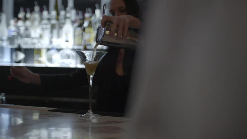 A bartender pours a drink into a martini glass from a shaker