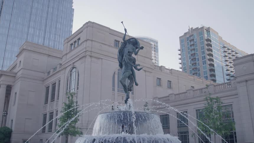Bronze statue of figure on horse with trumpet crowns urban fountain amid classical and modern architecture