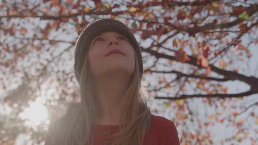 Girl looks upward beneath sunlit orange leaves