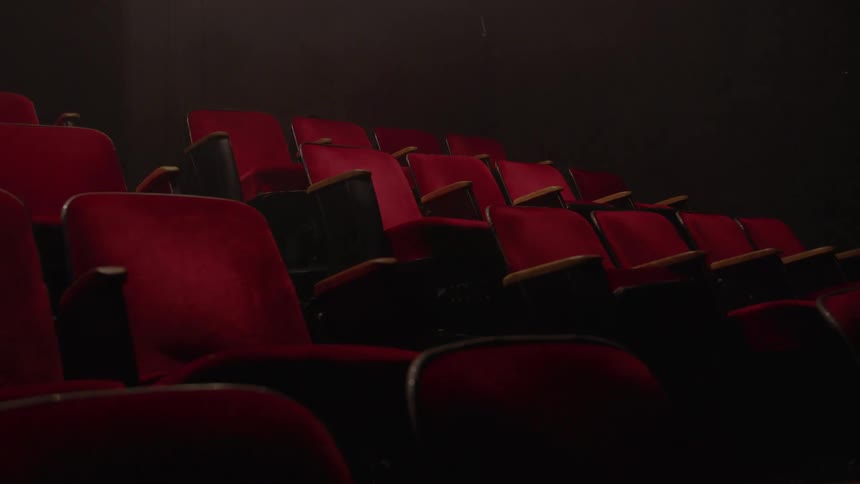Rows of empty plush red seats fill a dimly lit theater or cinema auditorium
