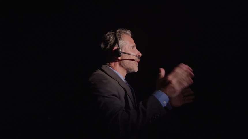 The face of a man wearing headphones in a completely dark environment making gestures and giving a lecture