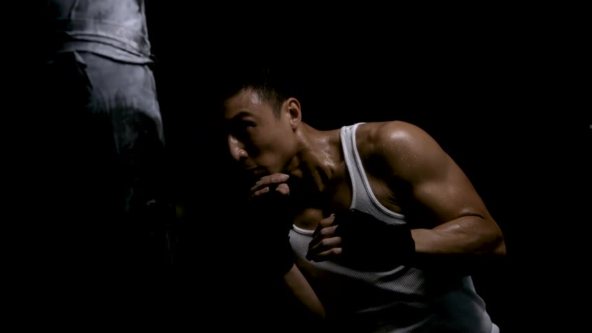 Muscular man with hand wraps trains boxing in dark intense setting