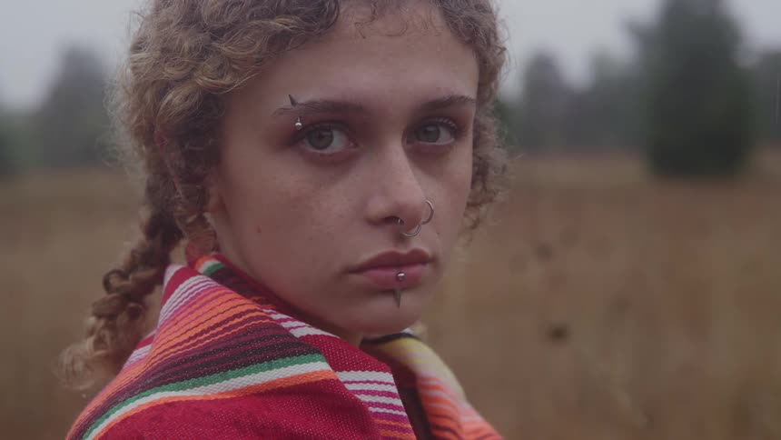 Young person with piercings and a colorful shawl looking directly at the viewer