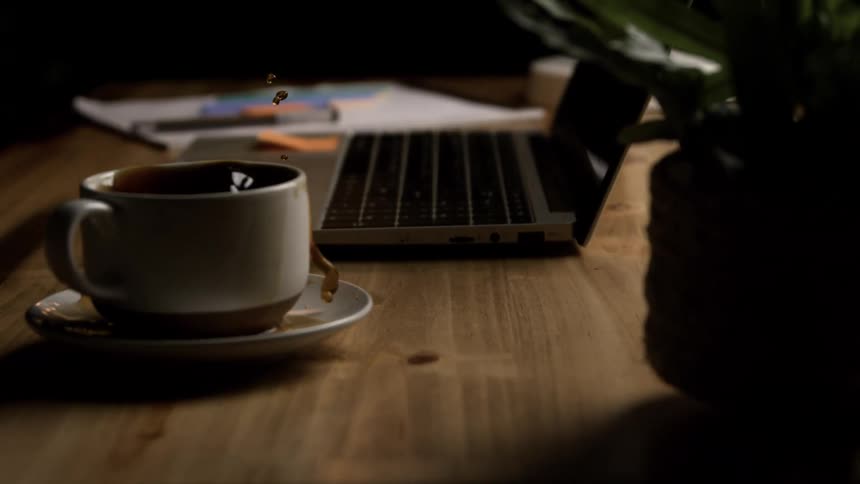 In slow motion a desk with a laptop shakes as if from an earthquake causing coffee to splash dramatically from a cup