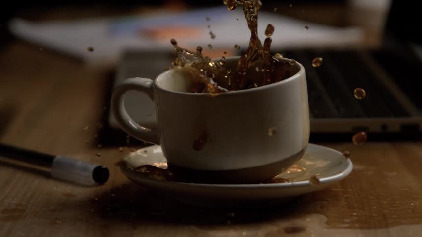 Coffee spills out of the cup creating splashes on the saucer and table