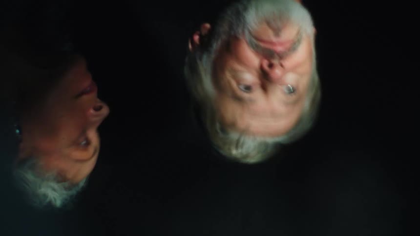 Blurred faces of two people appear upside down against a dark background