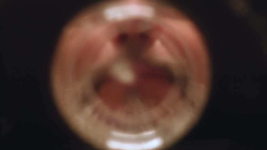 Viewed from inside a cup an older man spits out rinse water after brushing his teeth