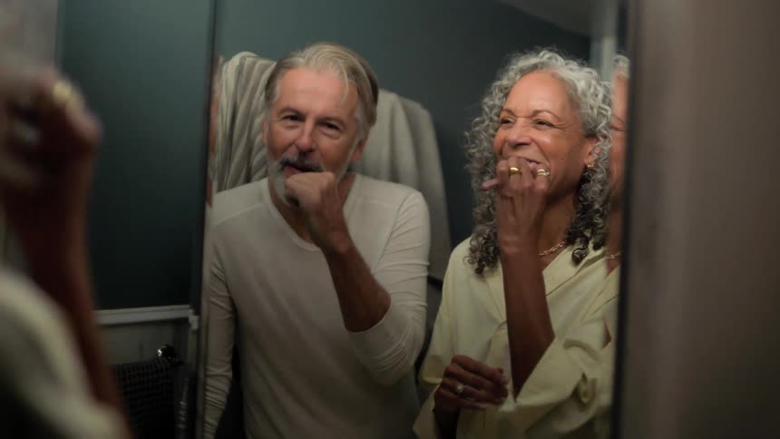 A man and woman brushing teeth in front of a mirror